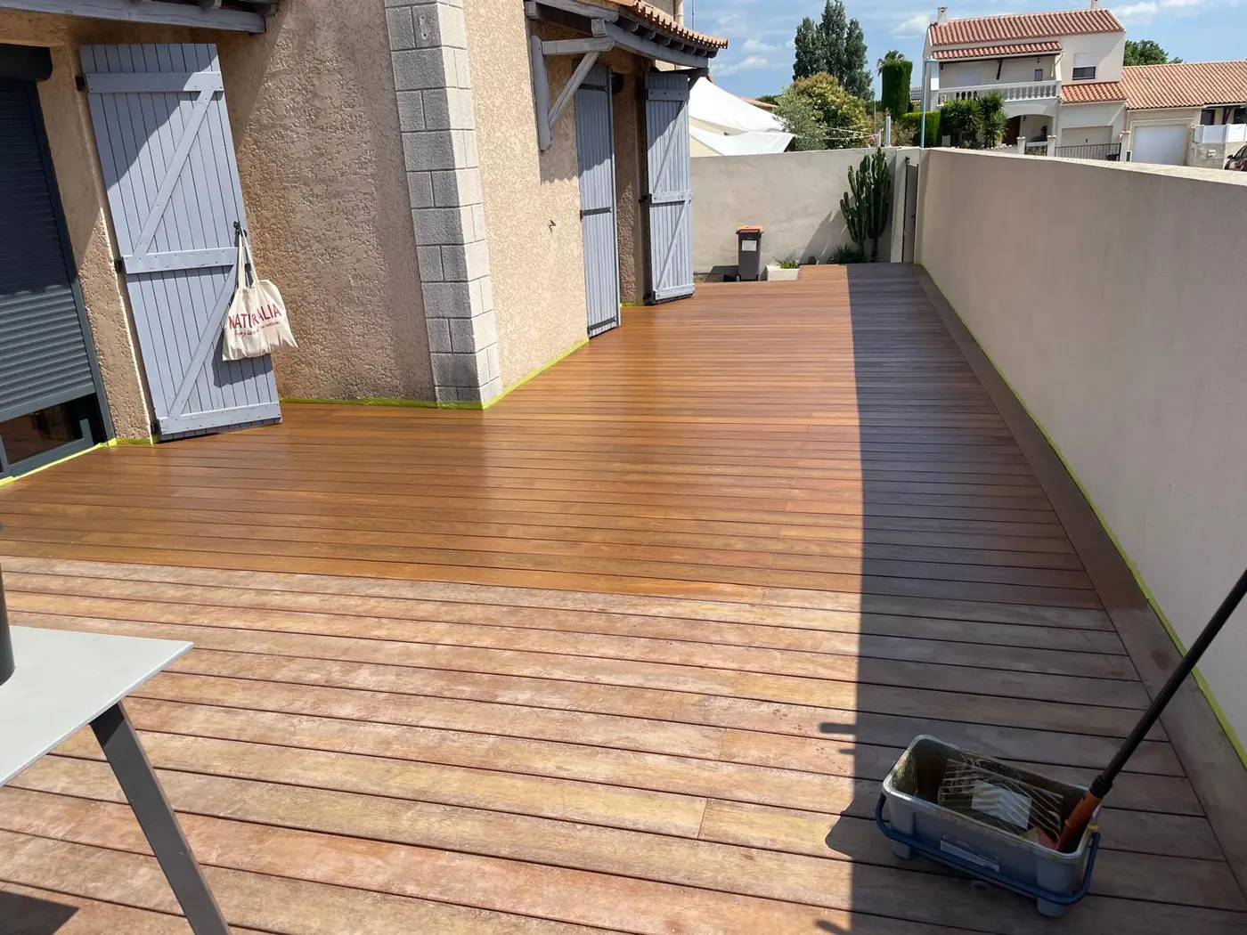 Terrasse en bois le long d'une maison, bac et pinceau posés à côté